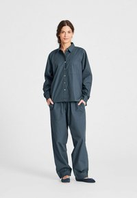 Camicia botton-down in cotone leggero di colore grigio scuro, con maniche lunghe e taschino sul petto, abbinata a pantaloni larghi abbinati con tasche laterali.