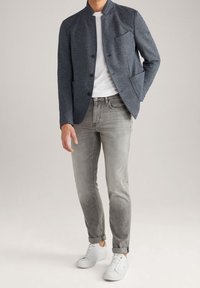 Navy textured jacket with a high collar, front pockets, and button closure, paired with gray tapered jeans and white sneakers.