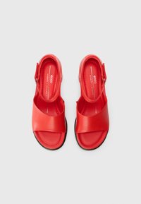 Red leather sandals with a wide front strap and ankle support. Flexible sole, minimalist design, and smooth texture. Brand logo visible inside.
