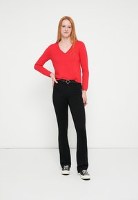 Suéter rojo de manga larga con escote en V combinado con jeans negros acampanados y zapatillas negras. El conjunto incluye un cinturón con hebilla plateada.