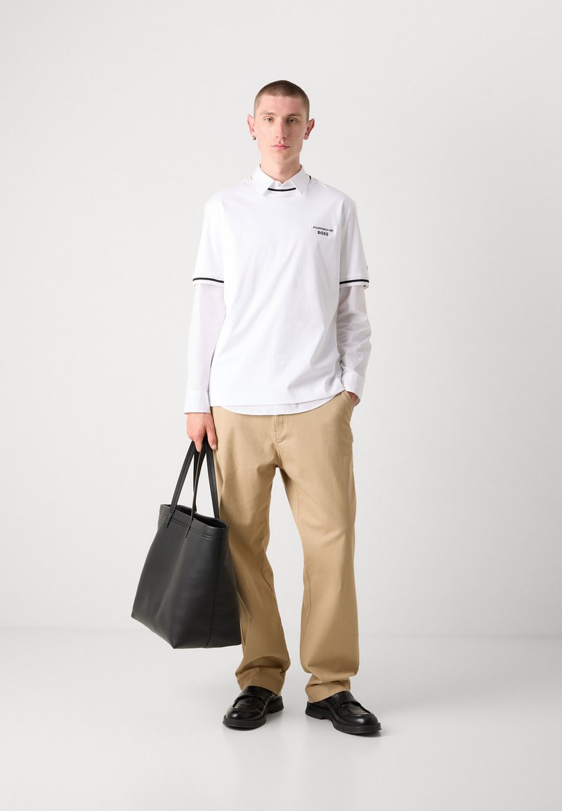 Polo bianco con strisce nere, pantaloni beige e borsa a tracolla in pelle nera. Il modello ha capelli corti ed indossa scarpe nere.