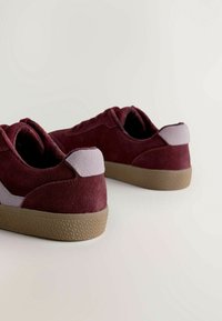 Baskets en suède bordeaux avec une semelle en caoutchouc brun texturé, présentant un accent gris clair au talon et un design lacé à profil bas.