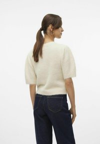 Crèmekleurige gebreide trui met korte, donzige mouwen en een zachte textuur. Draag met donkere denim jeans, achteraan gezien.