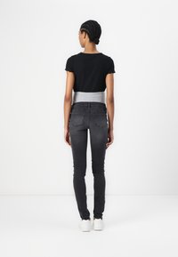 Top negro acanalado de manga corta, con una banda gris en la cintura, combinado con jeans ajustados gris oscuro y zapatillas blancas. Fondo blanco liso.