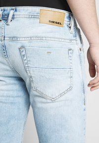 Ljust blå denimjeans har en läderlapp med "DIESEL"-logotypen, fem fickor och en något blekt textur med synlig sömnad.