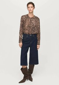 Blusa a stampa leopardata con spalle arricciate, abbinata a culotte in denim blu scuro a gamba larga e stivali in suede marrone fino al ginocchio.