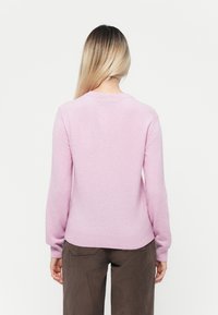 Lys rosa strikket genser med lange ermer og rund halslinning. Ribbestrikkede mansjetter og kant gir tekstur. Glatt overflate, avslappet passform.