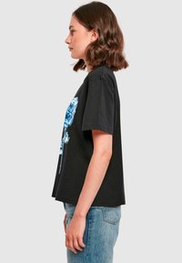 Sort bomulds T-shirt med et blåt rosegrafik foran, korte ærmer og en afslappet, kasseformet pasform. Båret med lyseblå jeans.