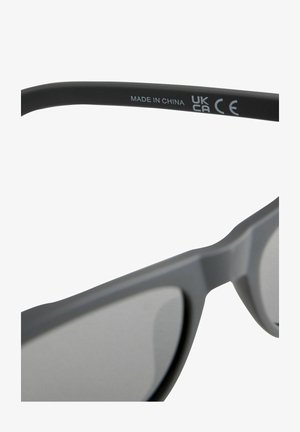 Szare okulary przeciwsłoneczne o matowym wykończeniu, z minimalistycznym wzornictwem i przyciemnionymi soczewkami. Oznaczenia obejmują "Wyprodukowano w Chinach", certyfikaty UKCA i CE.