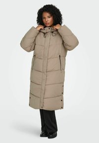 Garš bēšs pūcértā jakas ar kapuci, horizontālas šūtas joslas, divas sānu kabatas ar rāvējslēdzējiem un sānu aizdares ar spiedpogas ērtai valkāšanai.