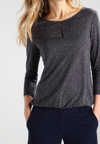 Marinblus med långa ärmar, vitprickig design, rund halsringning och liten nyckelhålsdetalj framtill. Mjuk, texturerad tyg.