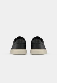 Sorte lærersneakers med avrundet form, beige gummisåler og minimalistiske aksentfarger i hvitt og oransje bak.