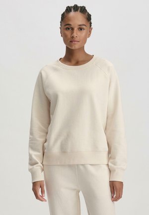 Felpa beige chiaro con colletto rotondo, polsini e orlo a coste. Texture morbida, vestibilità rilassata e maniche raglan.