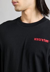 T-shirt nera a maniche lunghe in cotone, con un logo rosso "icecreaM" sulla parte sinistra del petto e design a collo rotondo.
