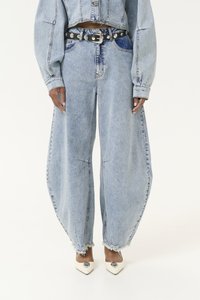 Jean en denim bleu clair à jambes larges, avec des ourlets effilochés et des coutures structurées. Associé à une ceinture noire et des escarpins blancs à bout pointu.