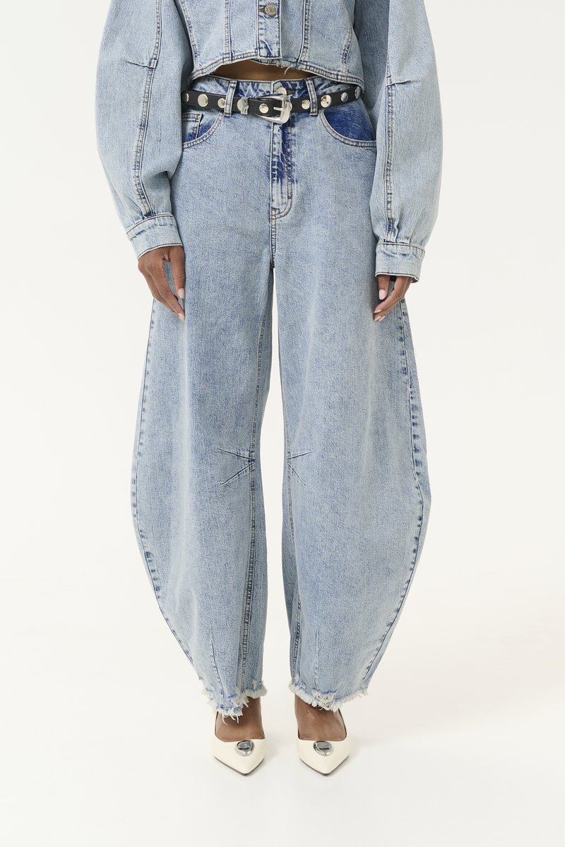 Jean en denim bleu clair à jambes larges, avec des ourlets effilochés et des coutures structurées. Associé à une ceinture noire et des escarpins blancs à bout pointu.