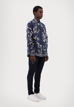 Navy button-up shirt with white floral embroidery, long sleeves, and a collar. Worn with dark jeans and white sneakers.
