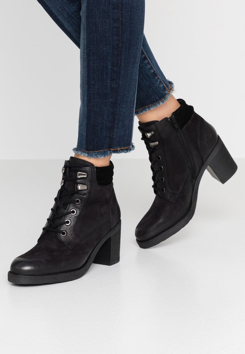 Botines negros hasta el tobillo con un acabado de ante texturizado, que presentan cordones, cremallera lateral y un grueso tacón cuadrado. Llevados con jeans ajustados.