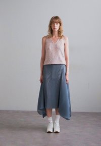Roze mouwloze top met pailletten, gecombineerd met een vloeiende blauwe plissérok en witte sneakers. Geplaatst tegen een eenvoudige, lichte achtergrond.