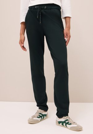 Pantalons de survêtement noirs, fuselés, avec une taille élastique et un cordon de serrage. Le tissu semble lisse et extensible, associé à des baskets grises et vertes.