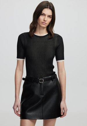 Top corto a maniche corte nero a coste con rifiniture bianche, abbinato a una gonna in pelle nera a vita alta con cintura e texture elegante.