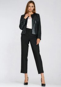 Czarna, cekinowa marynarka o prostym kroju, zestawiona z dopasowanymi czarnymi spodniami i jasnokolorową bluzką pod spodem.