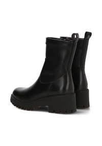 Botas de tobillo de cuero negro con un acabado liso, suela de goma gruesa y tiradores. Presentan un diseño elegante y minimalista con punta redondeada.