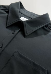 Black button-up shirt with a structured collar and a single pocket. Made of smooth fabric with subtle sheen and clean stitching details.