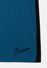 Koszulka sportowa Nike w turkusowym materiale z czarnymi siateczkowymi panelami bocznymi. Posiada czarną wyszywaną logo w lewym dolnym rogu.