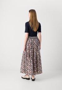 Tengerészkék és rózsaszín paisley mintás maxi szoknya, fitted toppal és réteges kialakítással, világos színű cipővel párosítva, semleges háttér előtt.