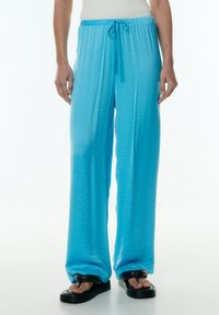 Lichtblauwe, wijde broek gemaakt van een gladde, lichte stof met een elastische tailleband en een verstelbaar trekkoord.