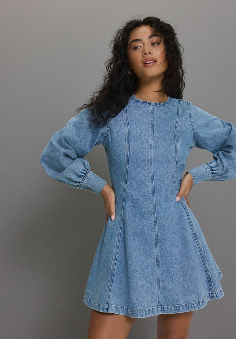 Denim kleit, millel on pikad puhv-sleeves, sinine värv, kitsas dekoltee, laienev seelik, ümmargune kaelus ja vertikaalne õmblusdetail.