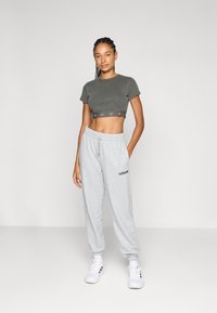 Šedý žebrovaný krátký top s krátkými rukávy a páskem s logem; světle šedé tepláky s logem, elastickým pasem a lemy u kotníků; bílé tenisky.