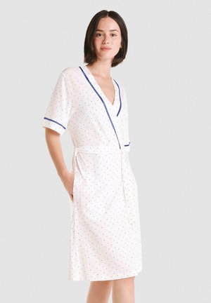 Bata corta blanca con lunares rojos y azules, escote en V, mangas cortas, ribete azul y cinturón con lazo; cuenta con bolsillos laterales.