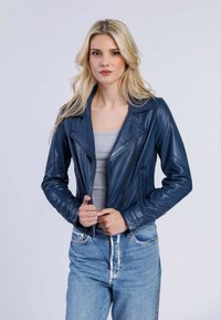 Giacca da motociclista in pelle blu con colletto a punta e chiusura a zip, abbinata a jeans chiari in denim e un top grigio. Texture liscia.