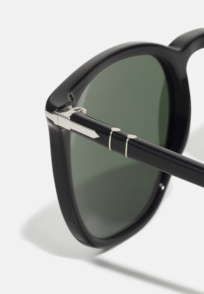 Black sunglasses with a square frame, green lenses, silver accents at the hinge and temple, and a glossy finish.