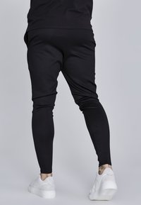 Čierne jogger nohavice vyrobené z hladkej, elastickej látky so slim fit strihom. V páre s bielymi teniskami na kontrast. Obsahuje manžety na členkoch.