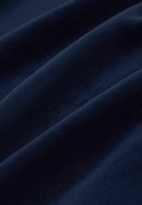 Tissu en velours bleu foncé avec des plis doux créant une texture lisse, moelleuse et des reflets lumineux subtils.