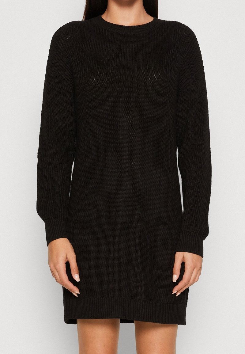 Abito nero lavorato a maglia con maniche lunghe, scollatura rotonda, polsini e orlo a costine. Ha una texture spessa e una vestibilità ampia.