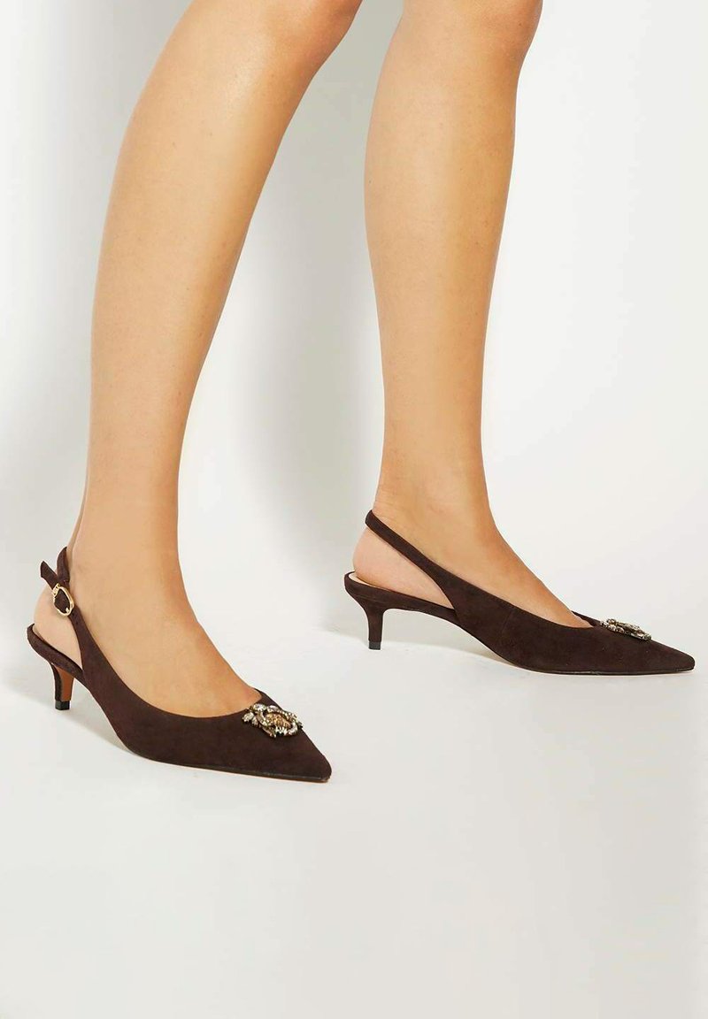 Brown suede slingback heels feature a pointed toe and small heel, adorned with a decorative brooch on the forefront.