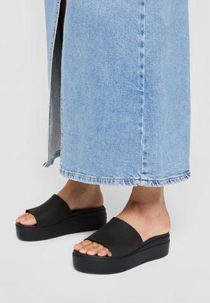 Pieds en sandales à plateforme noires à doigts ouverts, associés à une jupe en jean bleu clair avec une fente à l'avant.