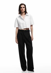 Witte cropped blouse met een kraag en een zak, gecombineerd met hoge zwarte wijde broek. Glad materiaal en een getailleerde pasvorm.