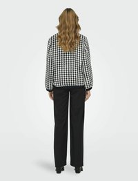 Giacca a motivo houndstooth bianco e nero con polsini elastici, abbinata a pantaloni neri a gamba larga e stivali con tacco, vista da dietro.