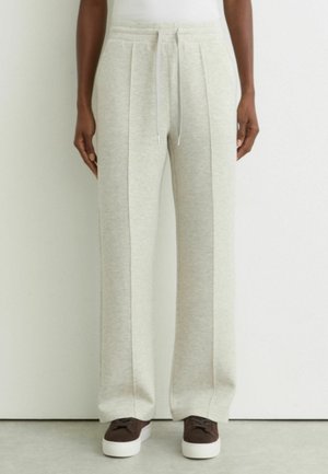 Person iført lysegrå vidde joggingbukser med fremadgående syninger, snøre i taljen og mørkebrune sneakers med hvide såler.