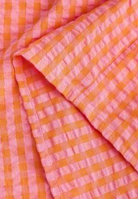 Bomuldsstof med skiftende lyserøde og orange gingham-firkanter. Teksturen virker blød med synlig syning langs kanterne.