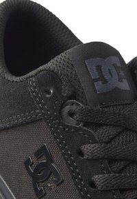 Černá sportovní obuv s texturovaným textilním svrškem a hladkým koženým překrytím, s výrazným logem a pevnými tkaničkami.