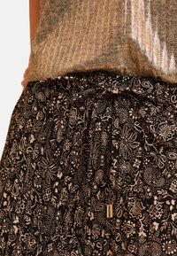 Zwarte rok met een bloemenpatroon, voorzien van een trekkoord in de taille en plooien. Gecombineerd met een metallic, gestructureerde top.