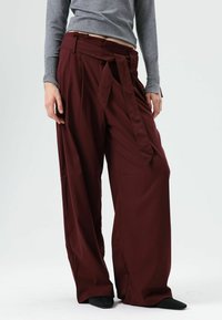 Wijde broek in bordeauxrode stof, met een tailleband met ceintuur, zachte textuur en strakke lijnen, gecombineerd met een grijs longsleeve top.