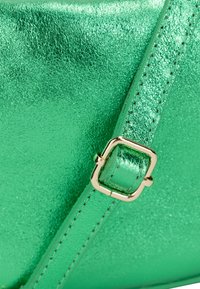 Sac à main vert métallisé avec une finition texturée, quincaillerie dorée et une forme structurée. Les accents incluent une boucle et une bandoulière cousue.
