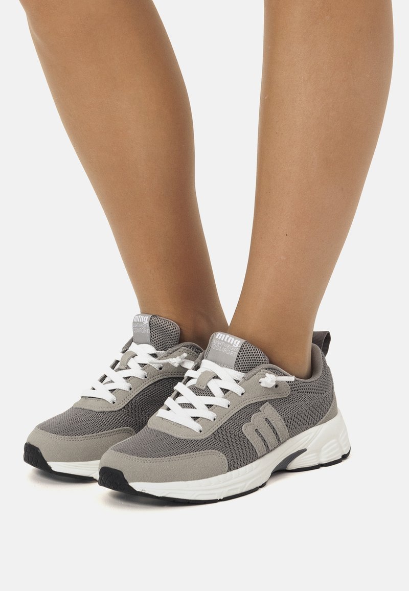 Zapatillas deportivas grises con parte superior de tela texturizada, cordones blancos y un diseño de suela acentuado. Cuentan con un collar acolchado para mayor comodidad.